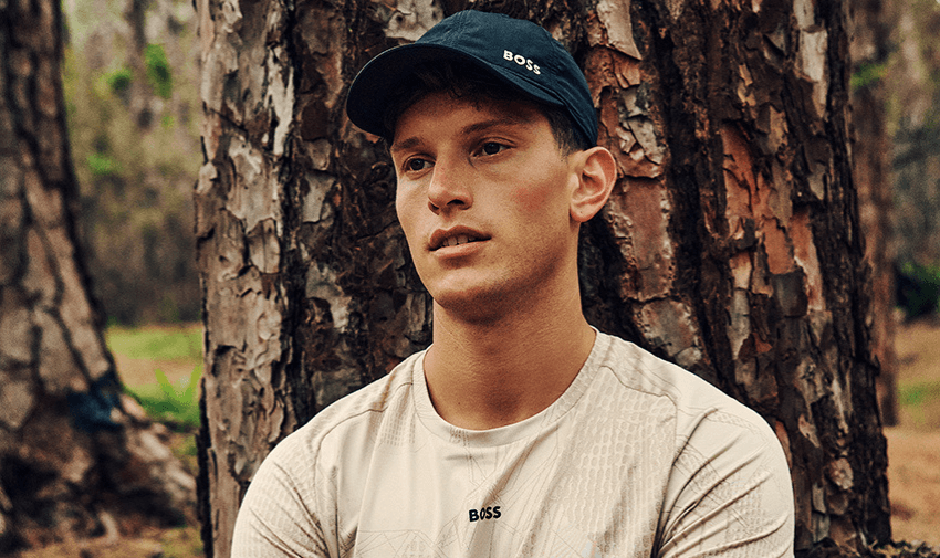 Man wearing a Hugo Boss cap and printed t-shirt sitting by a tree in a forest. Stylish menswear savings and accessible clothing deals for disabled people in the UK.