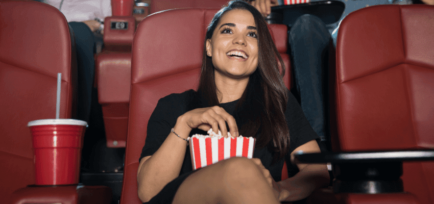 A woman enjoying a film at the cinema with popcorn in hand, seated in a plush red chair with a drink nearby – perfect for showcasing entertainment and accessible fun through Vue Disabled Cinema Discounts.