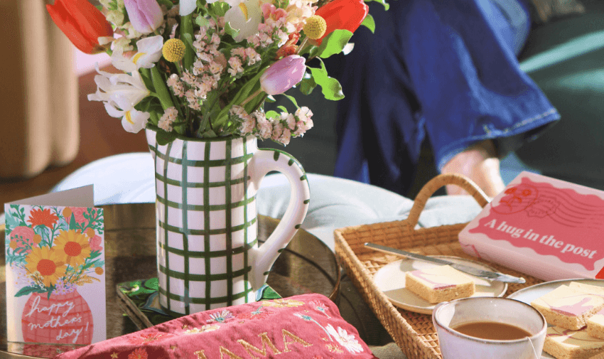 A Mother's Day setting with a jug of fresh flowers, a greeting card, tea, and biscuits on a tray, creating a cosy and welcoming vibe. Explore disabled discounts on flowers and gift deliveries.