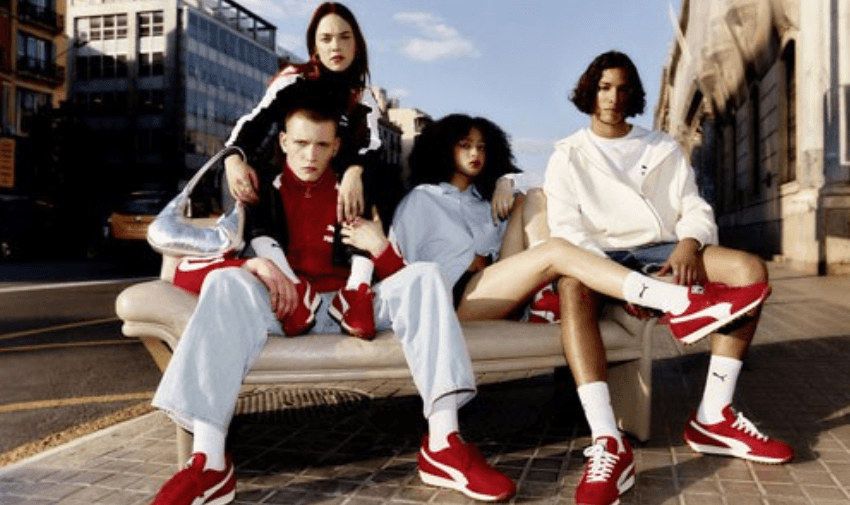 Four young adults posing in red PUMA trainers and urban streetwear on a sofa placed outdoors in the city, representing bold fashion and inclusive disabled footwear discounts available in the UK.