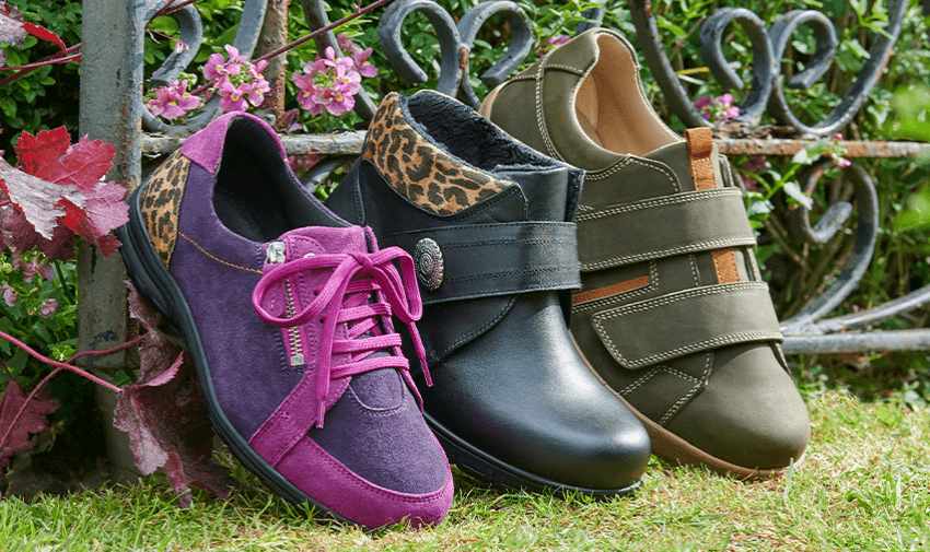 Three comfortable shoes on the grass, including a purple lace-up, a black ankle boot, and a green velcro shoe