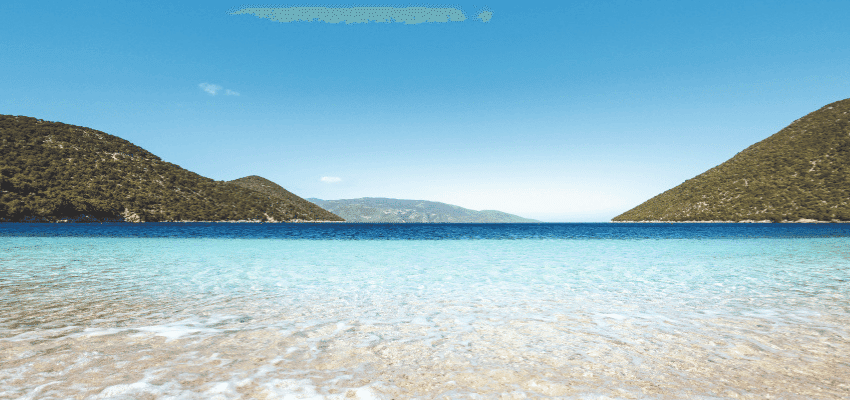 Clear blue sea and sandy shoreline between green hills on a sunny day Purpl discounts disabled travel discounts UK accessibility discounts UK savings for people with long term health conditions cost of living help for disabled people