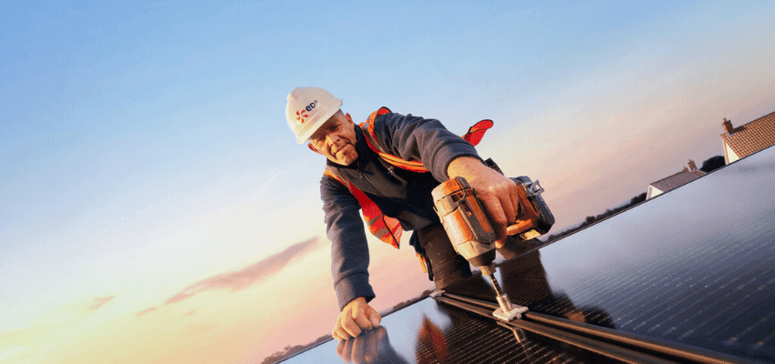 Engineer fits solar panel during sunset rooftop installation. Ideal for content on disabled homeowner energy discounts, accessible green energy savings and home upgrades.