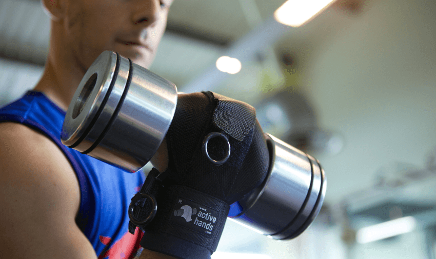 Disabled gym-goer using Active Hands gripping aid to lift a heavy dumbbell, highlighting inclusive fitness solutions and mobility discounts and offers.