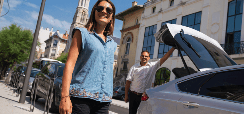 Woman smiling while a driver helps with luggage in a European city. Promotes accessible travel services, inclusive car transfers and disabled-friendly holiday experiences.