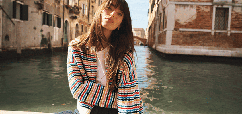 Woman wearing colourful Boden cardigan sitting by canal in European city promoting stylish fashion with disabled discounts in the UK