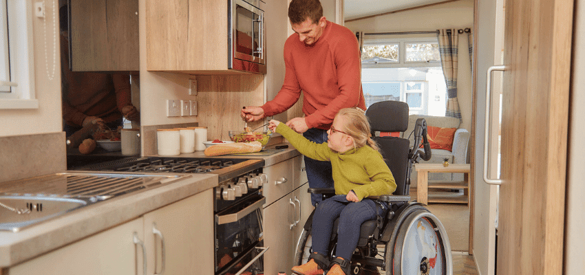 Father helps wheelchair user in kitchen at Parkdean Resorts, Purpl discounts for disabilities and long term health conditions, mobility discounts and offers.