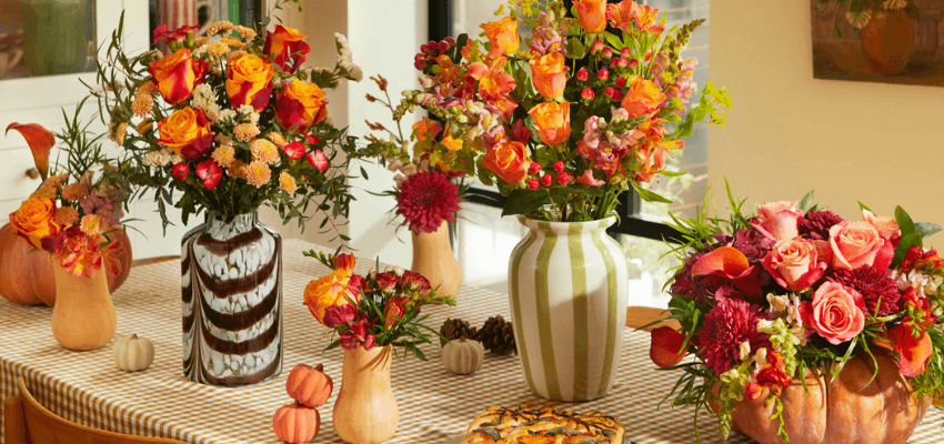 Autumn flower arrangements with orange roses, chrysanthemums, and greenery in decorative vases on a checked table, showcasing seasonal floral gifts. Keywords: Bloom and Wild Autumn Flowers, Seasonal Bouquets UK, Disabled Discounts on Flowers, Autumn Floral Gifts.