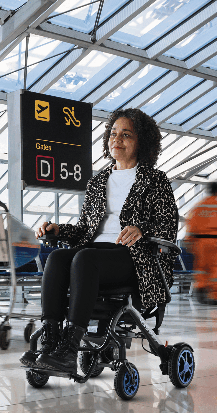 Woman with a long term health condition using a folding electric wheelchair at an airport terminal, highlighting accessible travel and mobility discounts for disabled people in the UK.