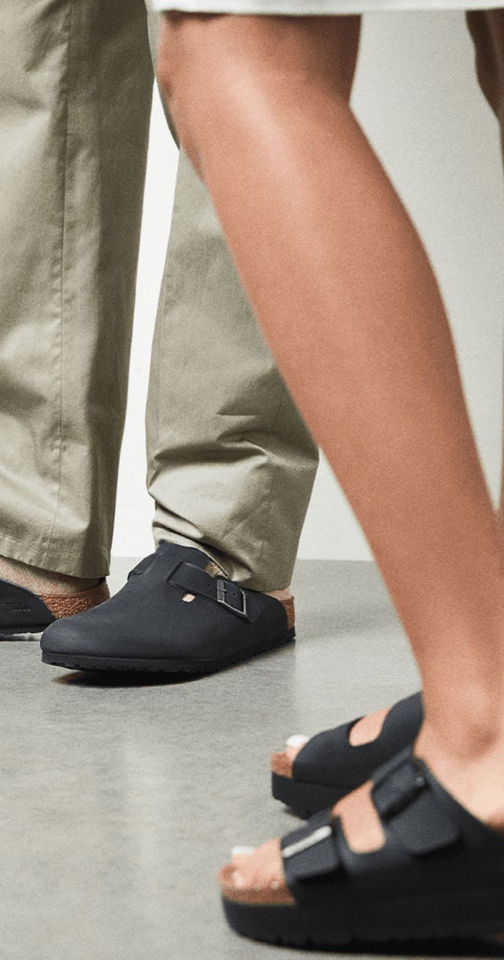 Close-up of two people wearing Birkenstock sandals and clogs in black with cork soles, styled with casual outfits, showcasing comfortable footwear discounts and everyday fashion offers for disabled people.