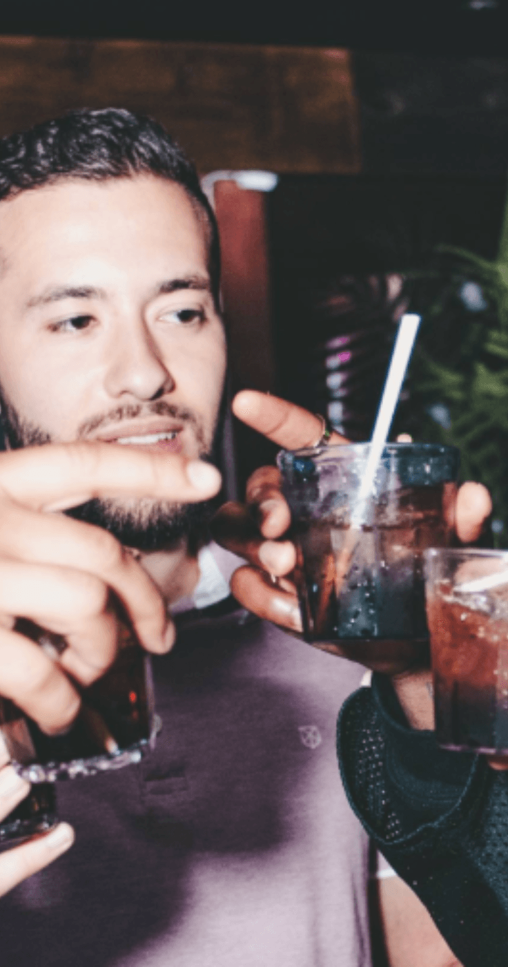 A group of friends clinking glasses filled with drinks in a lively bar setting, showcasing The Bottle Club. Highlighting Purpl's exclusive discounts on beverages and social experiences for disabled people in the UK.