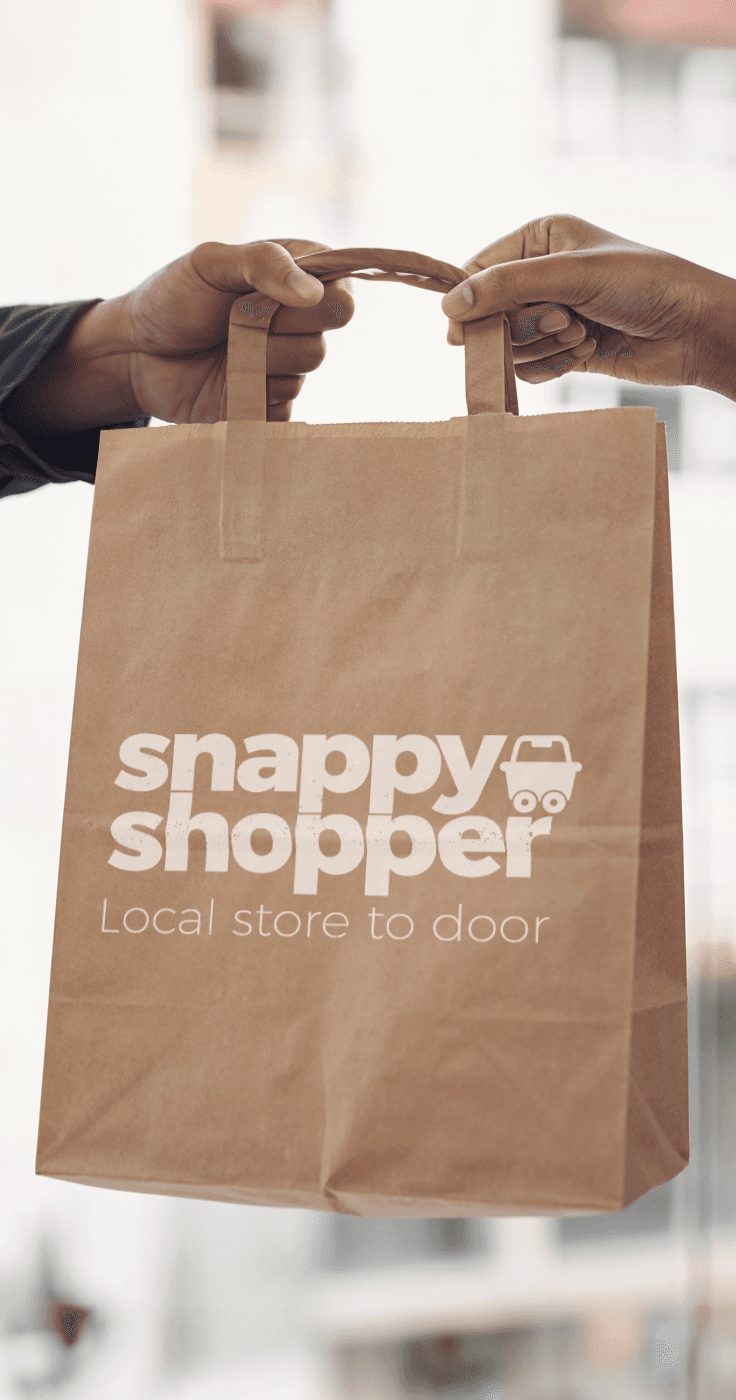 Close-up of two hands exchanging a paper bag with Snappy Shopper logo and ‘Local store to door’ slogan printed on the front, highlighting accessible shopping delivery for disabled people in the UK.