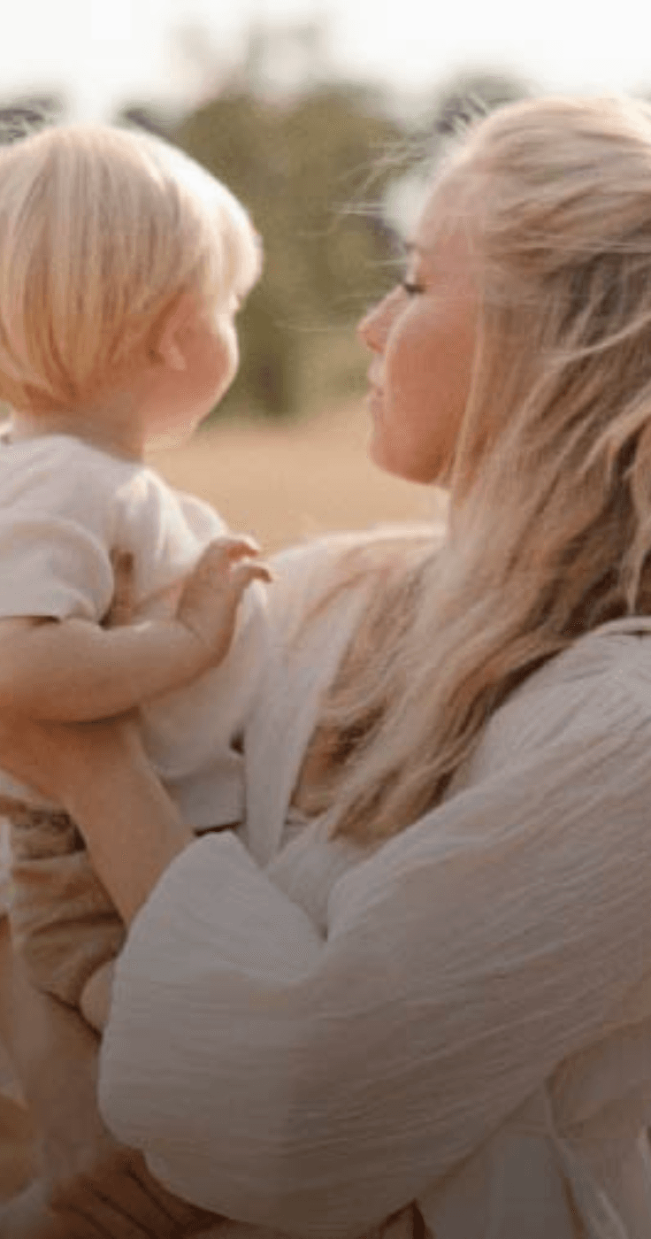 A mother holding her toddler in a golden wheat field, both gazing into the distance. Highlights Shopping Discounts for Disabled Parents and Baby Products Discounts.