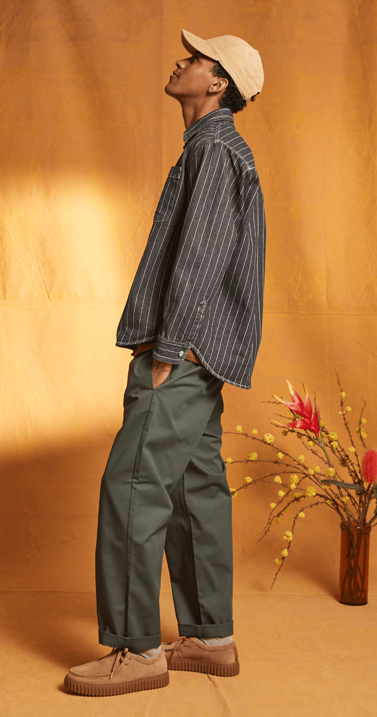 Trendy man in a striped shirt, cap, and green trousers styled with casual trainers, showcasing The Hut menswear collection with affordable fashion discounts and exclusive clothing offers.