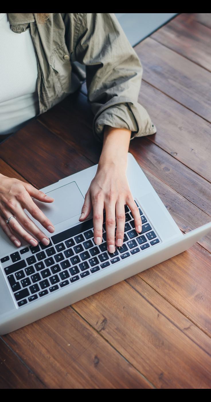 Close-up of a person's hands typing on a silver laptop with black keys. 