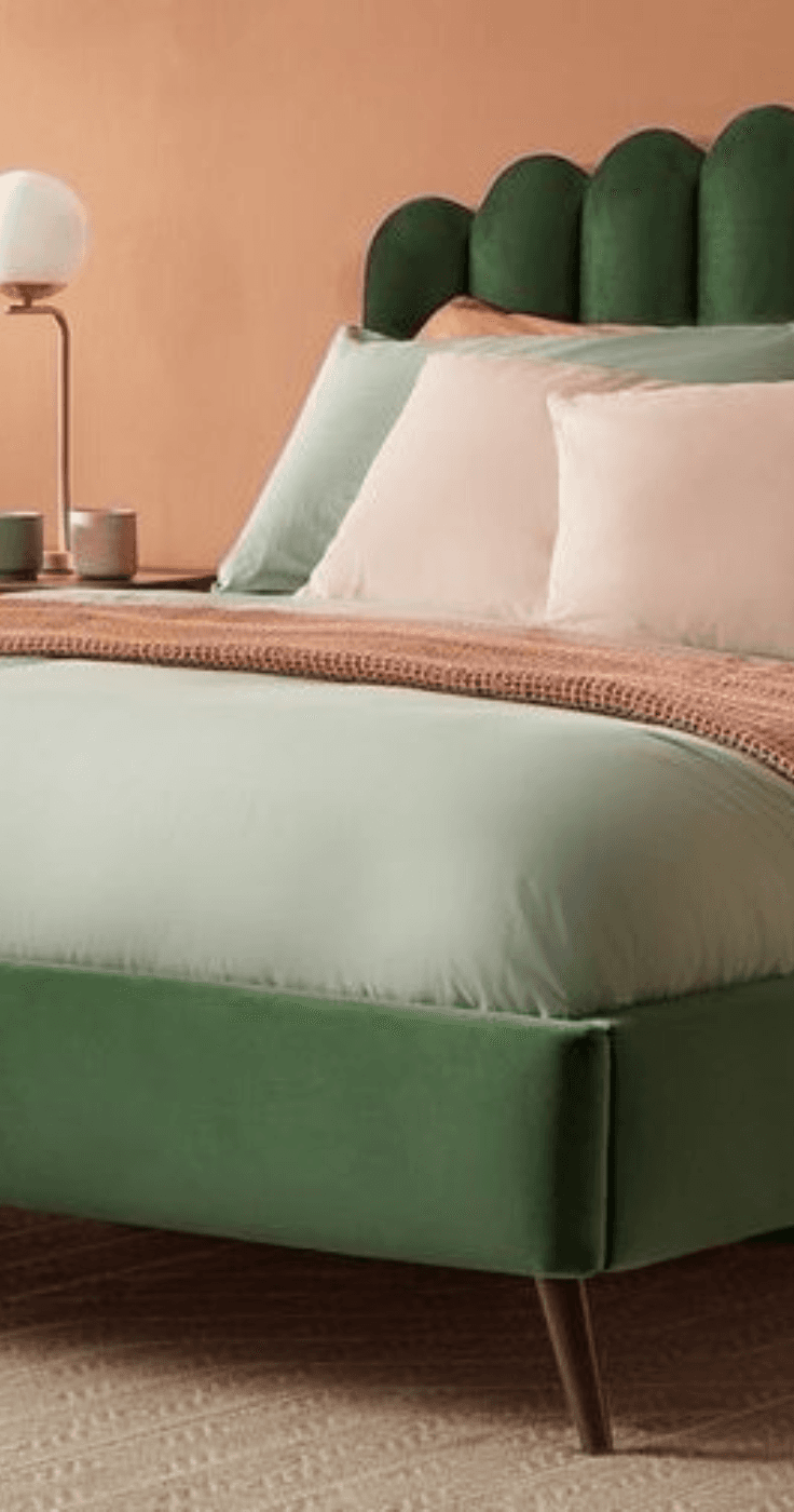 A modern bedroom with a green velvet bed against a warm-toned wall. The bed is neatly dressed with a soft pastel duvet and pillows, creating a relaxing atmosphere. Disabled Home Essentials Savings, Accessible Furniture Deals UK.
