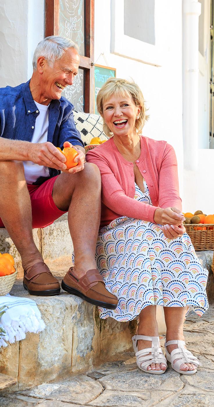 Older couple in breathable Cosyfeet footwear smiling in the sun while on holiday, ideal summer shoes for swollen feet, mobility shoes for elderly, and wide fit sandals for disabled people.