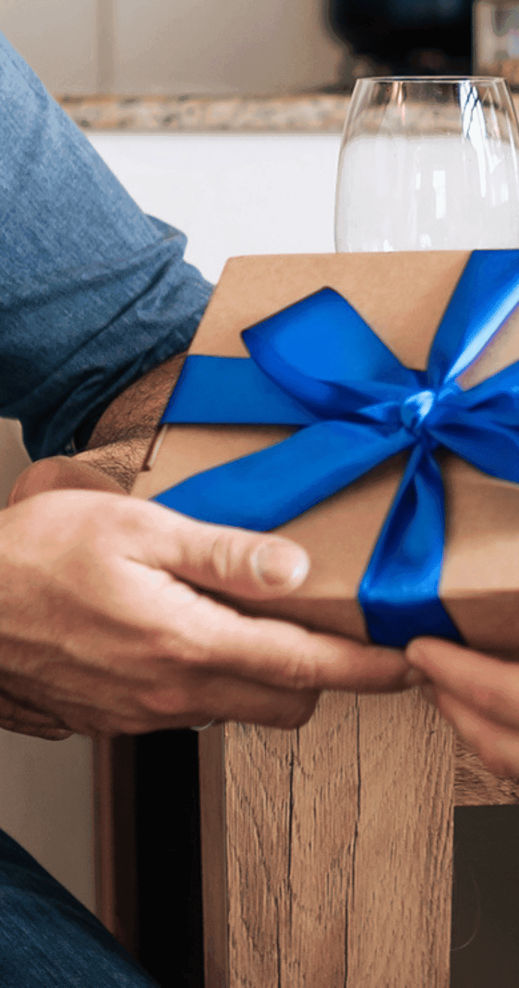 A person hands over a brown gift box tied with a bright blue ribbon, showing a close-up moment of gifting. Great for Gift Discounts for Disabled People and Disability Gift Ideas UK.