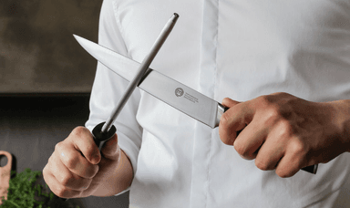 A chef in a white uniform sharpens a professional MasterChef knife using a honing steel, demonstrating precision and quality in culinary tools. Save on Kitchen Essentials for Disabled People.
