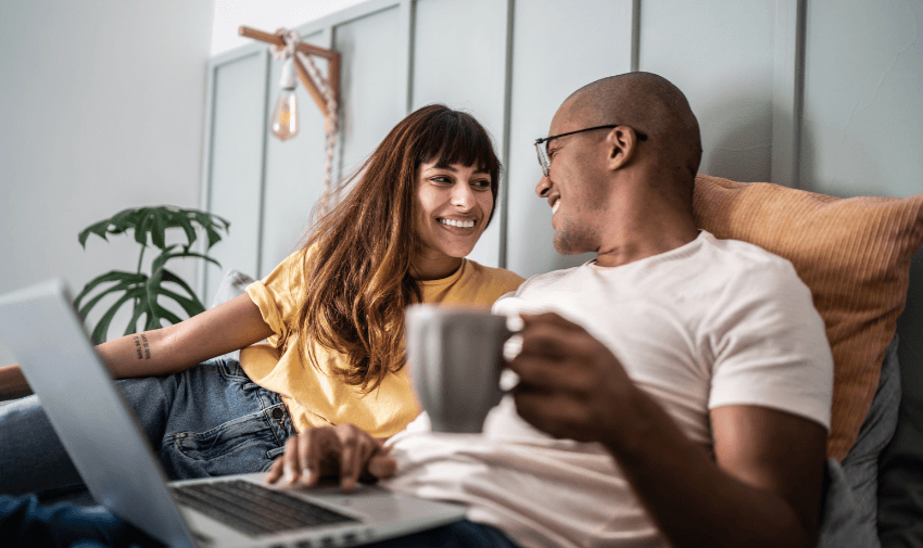 A smiling couple sitting on a sofa, looking at a laptop together, illustrating exclusive disabled member deals.