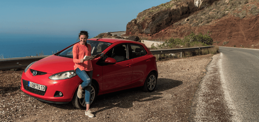 Woman leaning on red car by coastal road, Holiday Extras Purpl discounts for disabilities and long term health conditions, disabled travel discounts UK.