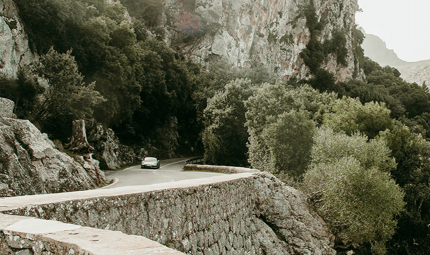 A car driving through a picturesque rocky pathway with greenery and cliffs, embodying stress-free journeys enabled by reduced excess costs. 