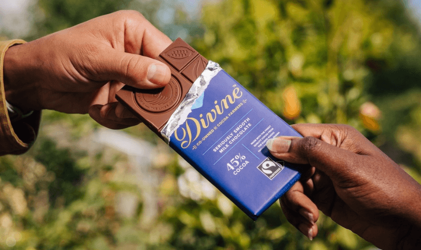 Two hands sharing an opened Divine Seriously Smooth Milk Chocolate 45% Cocoa bar outdoors, highlighting indulgent Fairtrade chocolate deals and inclusive shopping discounts for disabled people.