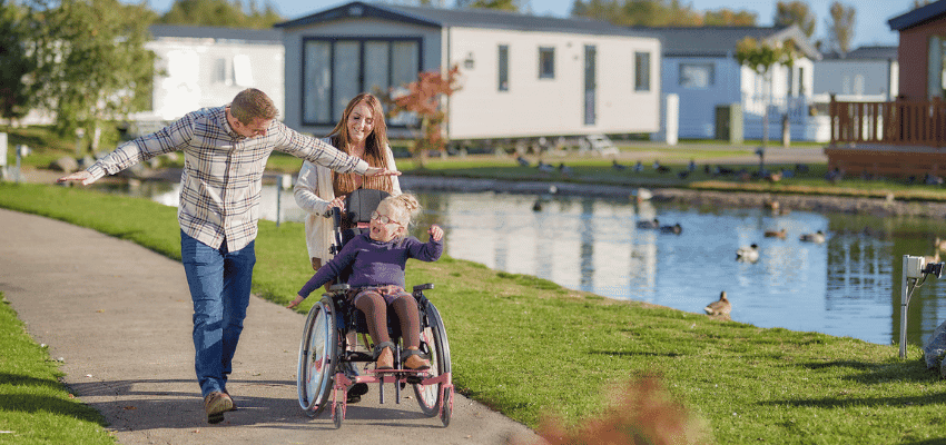 Family pushing wheelchair by lakeside at Parkdean Resorts, Purpl discounts for disabilities and long term health conditions, disabled travel discounts UK.