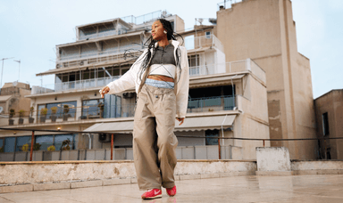 Young woman dancing in pink Nike trainers and relaxed loungewear on a rooftop, showcasing inclusive fashion with mobility discounts and disabled student offers