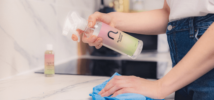 Person spraying Natrie all purpose cleaner onto a kitchen worktop and wiping it with a blue cloth.