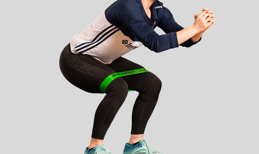Woman squatting with a green Physique resistance loop band around her thighs, highlighting affordable adaptive fitness accessories and accessible mobility workouts for disabled people in the UK.