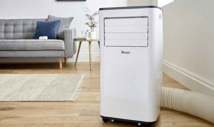 White Swan portable air conditioning unit with exhaust hose set up in a modern living room with wooden floors, grey sofa, and minimalist decor, offering home cooling solutions with household discounts for disabled people in the UK.