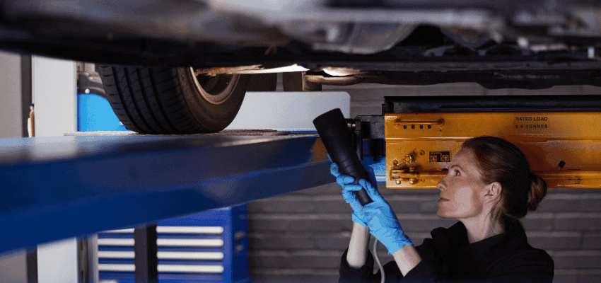 A mechanic inspects the underside of a car during an MOT, shown in a Halfords Autocentre workshop, linked to Purpl discounts for people with disabilities and long term health conditions who need affordable vehicle maintenance.