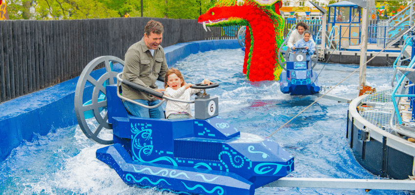 Father and child smiling on a blue water ride with a dragon sculpture in the background at LEGOLAND® Windsor. Promotion for Purpl’s LEGOLAND disabled discounts, including accessible ride options, companion ticket offers, and mobility support for family days out.
