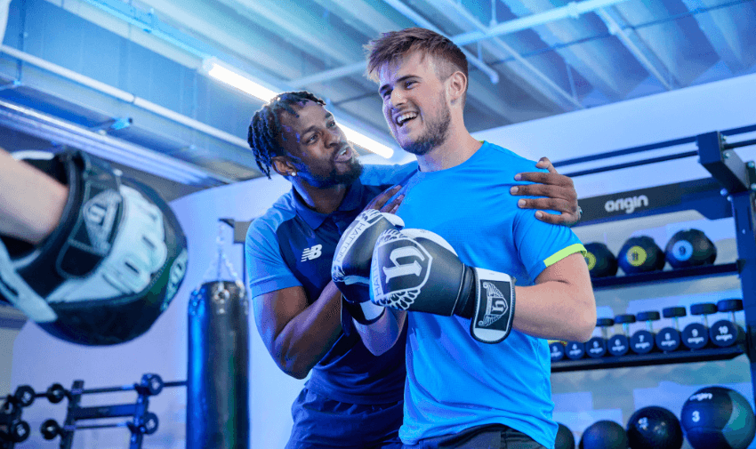 Boxing trainer coaching a smiling man wearing gloves at The Gym Group gym, representing accessible fitness programmes and shopping discounts for disabled people in the UK
