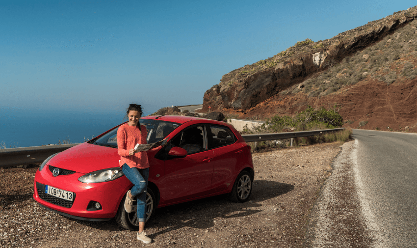 Woman reading a map while leaning on a red hire car by the coast. Great for promoting disabled-friendly car hire, accessible road trips and inclusive holiday transport.