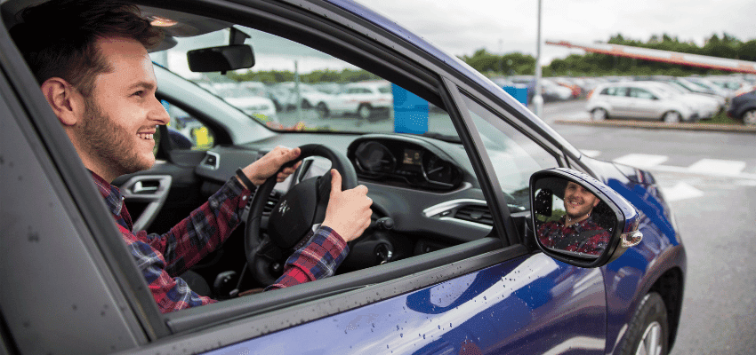 Smiling driver in blue car at car park, Holiday Extras Purpl discounts for disabilities and long term health conditions, disabled travel discounts UK.