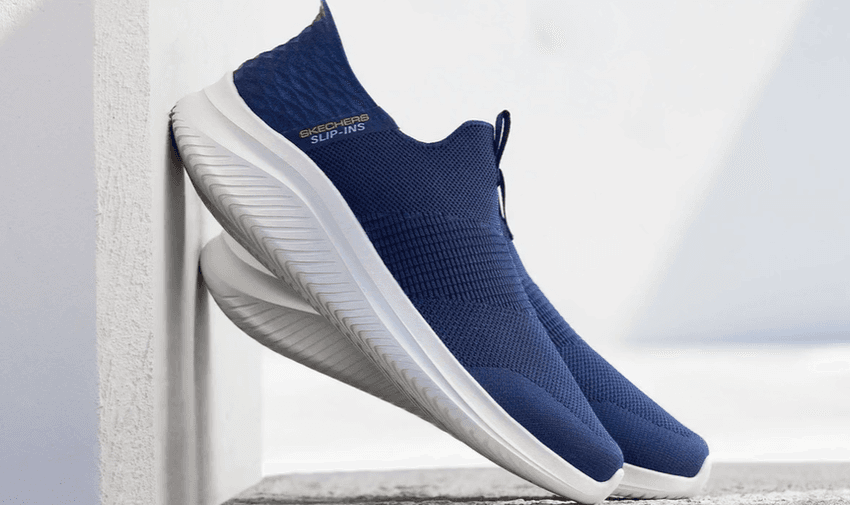 Pair of navy blue Skechers slip-on trainers with white soles leaning against a wall – hands-free slip-ins with disabled shoe discounts offering comfort, convenience, and easy wear for mobility support.