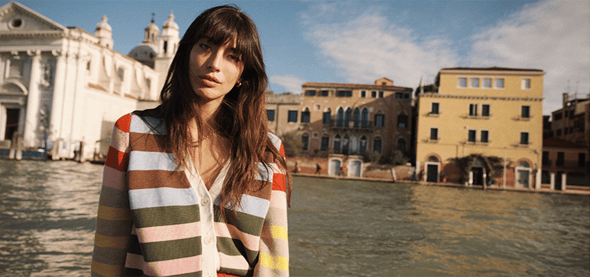 Woman wearing striped Boden cardigan standing by waterfront in European city promoting stylish fashion offers with disabled discounts in the UK