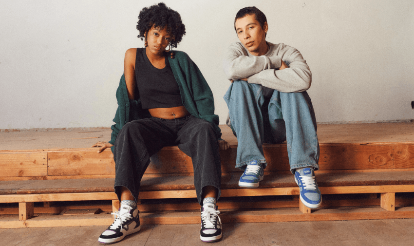  Two young adults sitting on wooden steps wearing Vans trainers, one in black and white and the other in blue and white, styled in casual streetwear, promoting fashionable and accessible footwear discounts for disabled people in the UK.