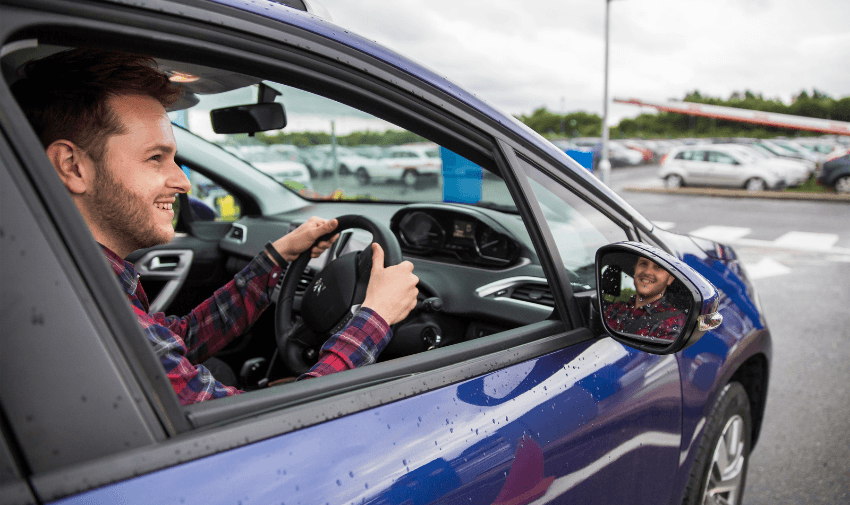 Man smiling from the driver’s seat at an airport car park. Highlights easy overseas airport transfers with mobility support and inclusive disabled transport offers.