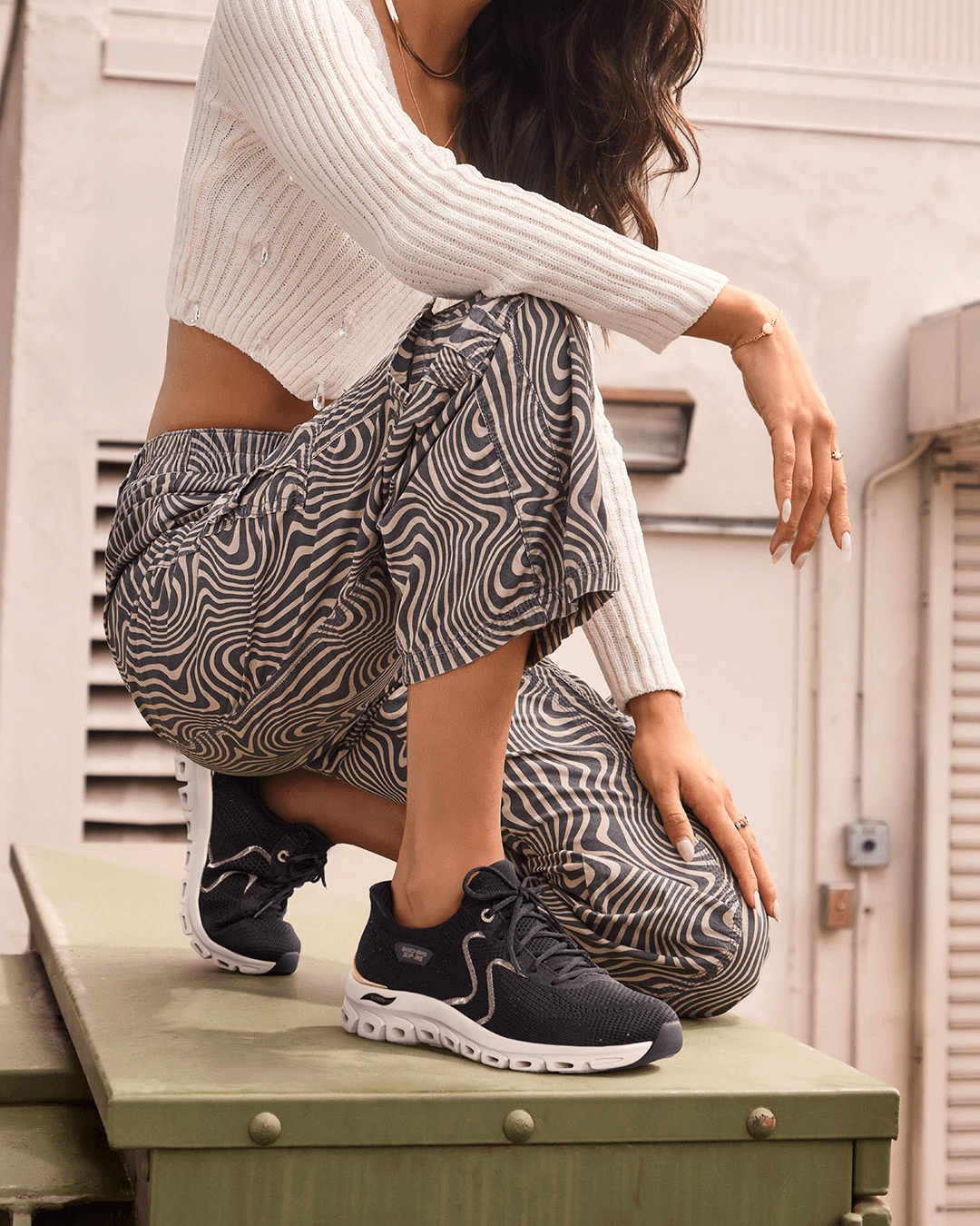 A woman kneeling down wearing dark trainers and patterned trousers