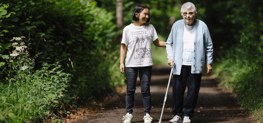 Carer walking with elderly woman using a stick in the park, Trinity Homecare Mobility Discounts UK and Carer Savings Offers.