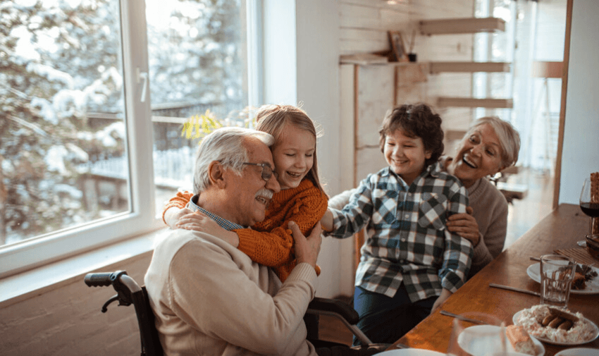 Grandparents and children smiling around the table, winter scene outside. Perfect for content about family energy savings, winter bills, and inclusive home energy support for disabled people and older adults.
