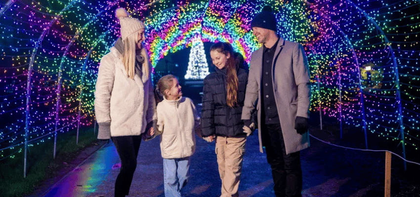 Family walking through a rainbow-lit tunnel at Warwick Castle’s festive light trail. Highlights accessible winter attractions and family-friendly events available with Purpl’s disabled discounts in the UK.