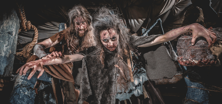 Two actors in Victorian costumes carrying a large wooden crate in a dark alley scene at The Edinburgh Dungeon, UK disability discount offers.