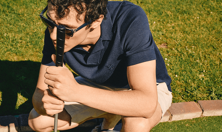 A man in sunglasses holding a golf club, crouching on a golf course, highlighting shopping discounts for disabled people.
