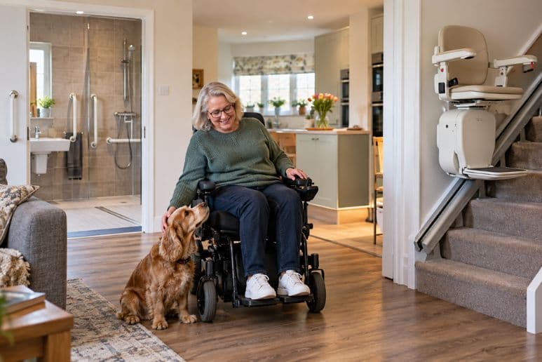 Disabled woman using a powered wheelchair in an adapted UK home with a stairlift and accessible bathroom.
