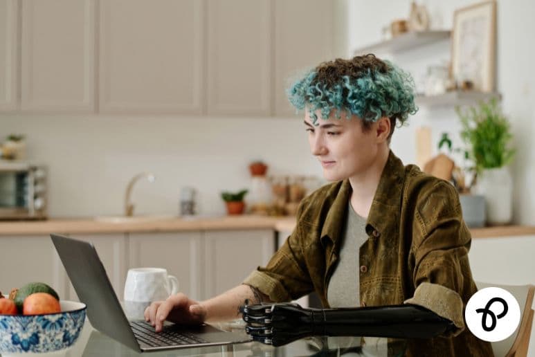 Person with a prosthetic arm working on a laptop while managing disability related costs, long term health conditions and Purpl discounts.