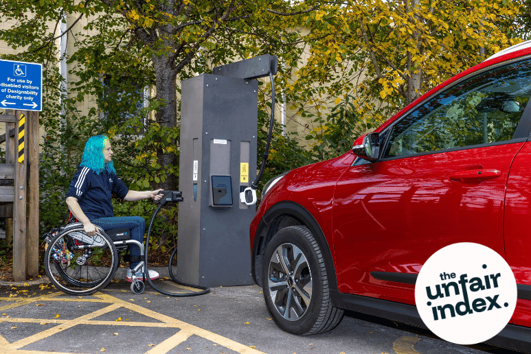 Wheelchair user charging an electric car in a disabled parking space showing accessibility and design barriers for people with disabilities and long term health conditions.